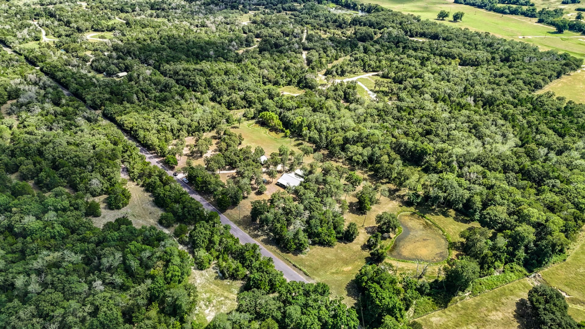 Aerial view of the 7.4-acre property with farmhouse, pond, and mature oaks near Independence, Texas